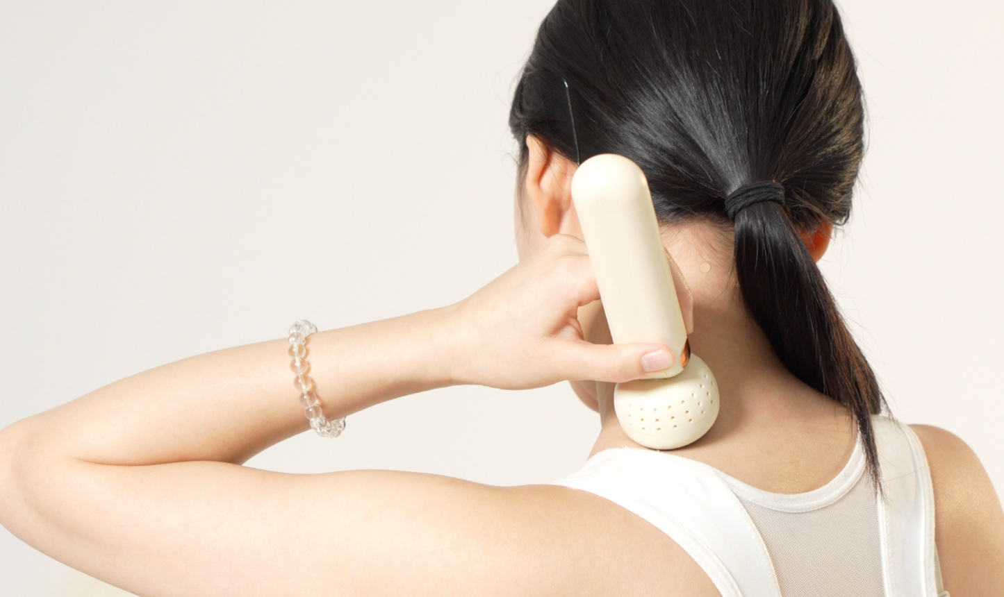 Woman using a white handheld device on her neck against a plain background