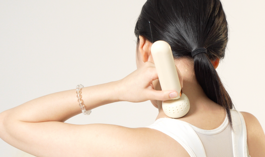 Woman using a white handheld device on her neck against a plain background