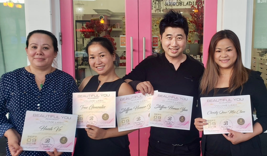 Four people holding certificates in front of a pink door with glass panels.